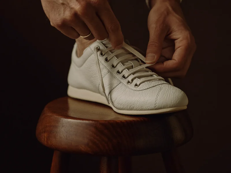 Mani che allacciano una sneaker su uno sgabello in legno, dettaglio della pelle